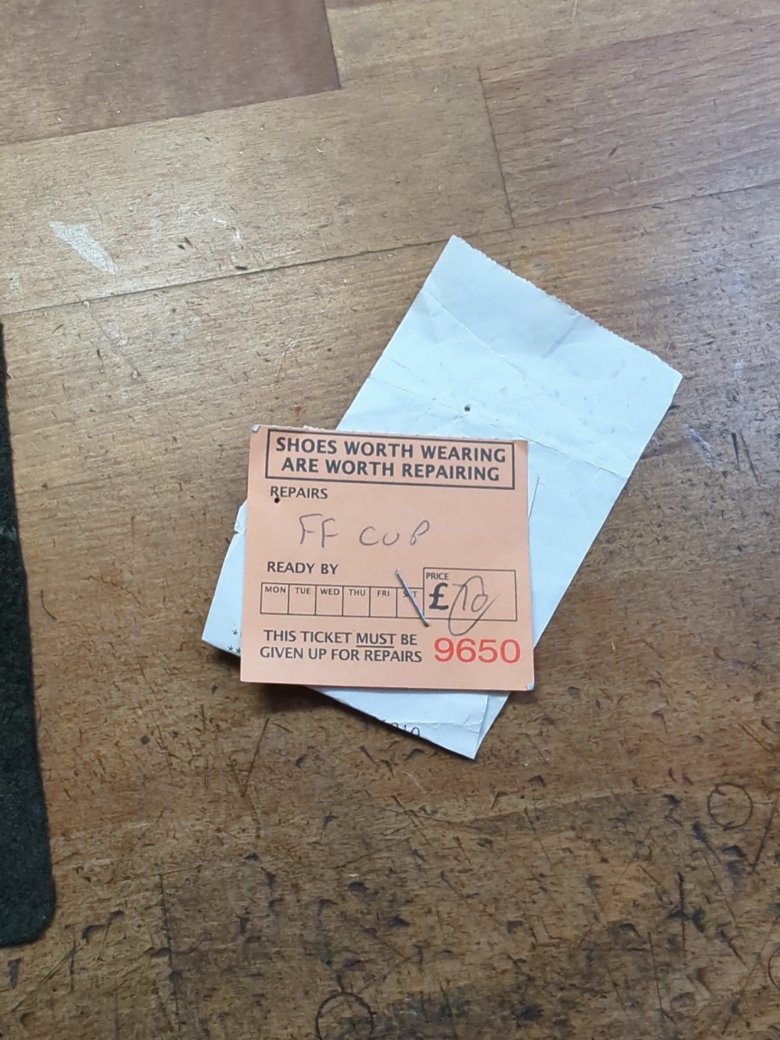 A traditional orange repair ticket on the workshop bench reading Shoes worth wearing are worth repairing.
